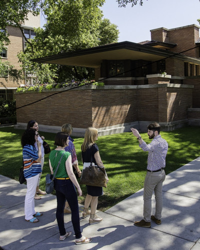 A group stand on the pavement outside the Robie House in Chicago